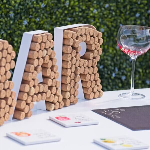 Close of of a bar sign made up of corks sitting on top of a white mobile bar. A colourful gin glass and coasters and bar runner are seen beside the sign