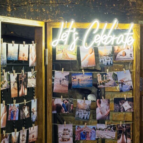 Close up of photos being displayed on photo wall with a bright LED "Let's Celebrate" sign