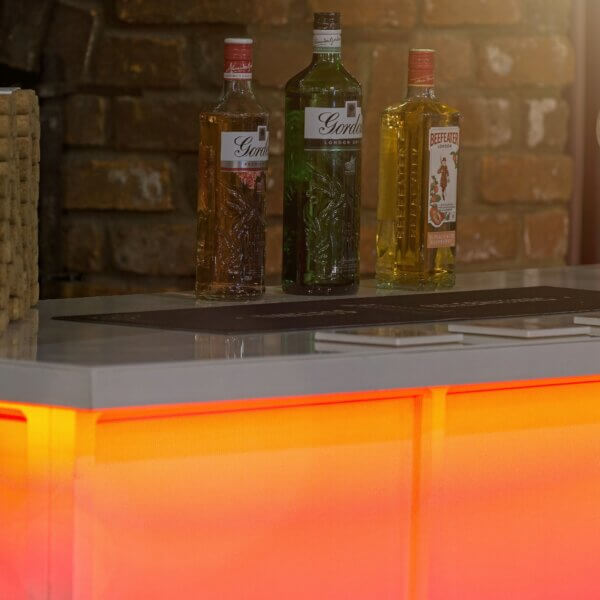 Close up of 3 alcohol bottles sitting on top of an LED bar. a red glowing light is visible underneath the bar worktop