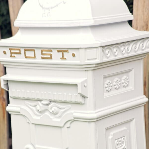 Right side angle of the white metal post box. Gold writing visible saying "Post" at the top and post flap also visible.