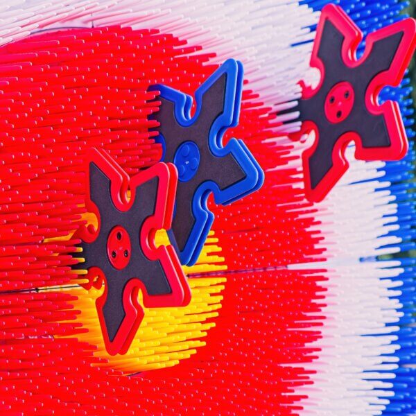 Close up of red and blue plastic throwing stars. The 3 stars are embedded into the axe throwing target, near the centre bulls eye.