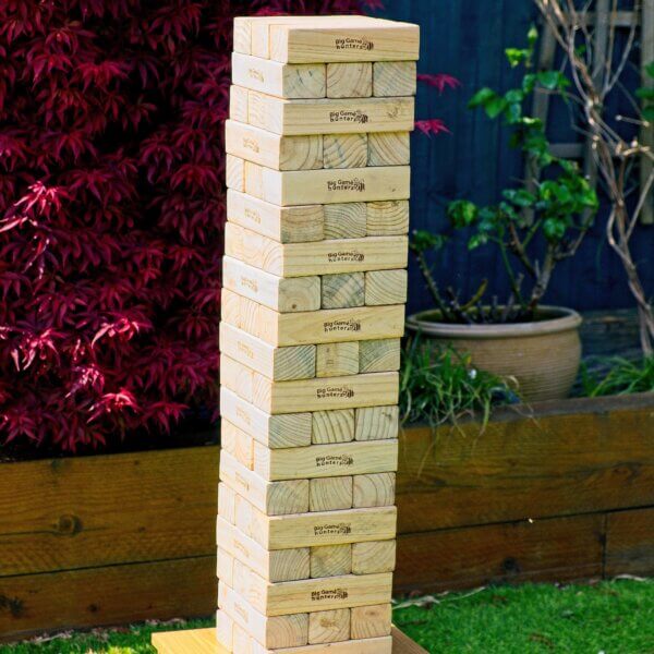 Giant Jenga tower sitting on top of a small wooden table outside. The wooden blocks are arranged 3 blocks per row and the next row is turned 90 degrees. The tower stands at 19 rows high.