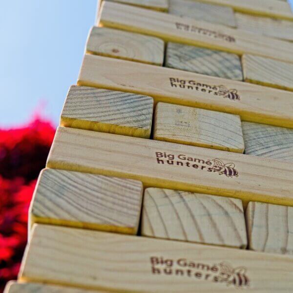 Close up photo of Giant Jenga tower, looking upwards at the tower. About 5 rows are visible and the top of the tower is not visible. Each row has 3 bricks and each row is turned 90 degrees to the previous.