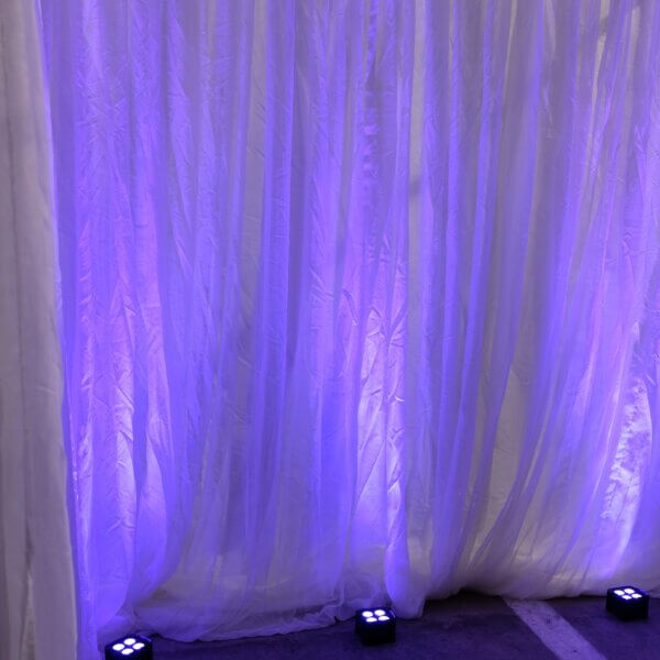 3 black, small, battery uplighter shown on the floor shining purple light up at white drape backdrop.