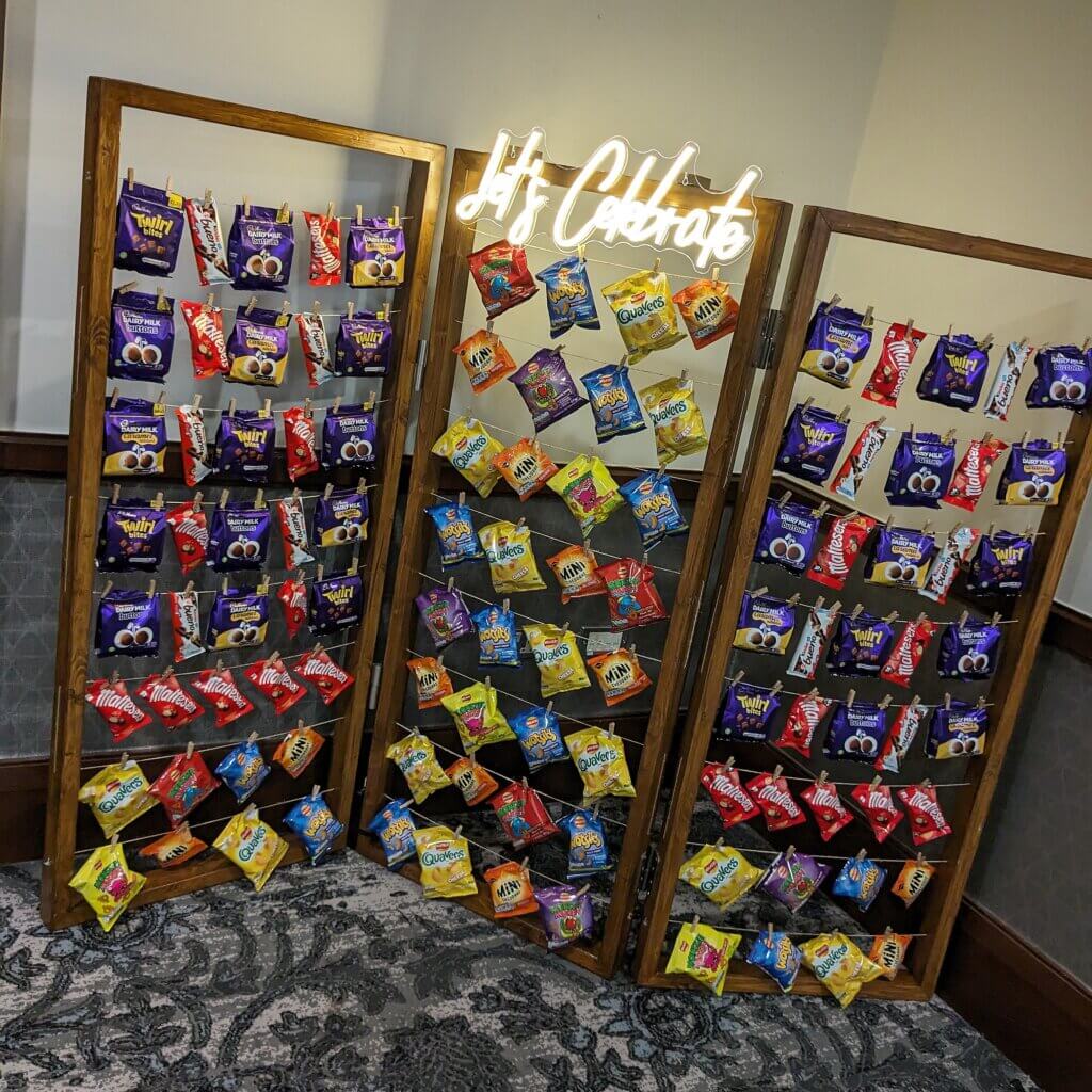 Various crisps and snacks, including chocolates, being displayed on crisp wall with LED "Let's celebrate" sign at Norton Park Hotel