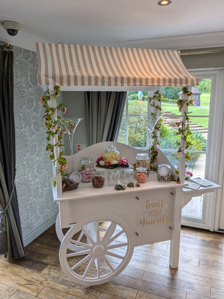 Sweet cart with gold and white top canvas, sign saying "Treat Yourself" and matching bags. Jars are filled with various sweets