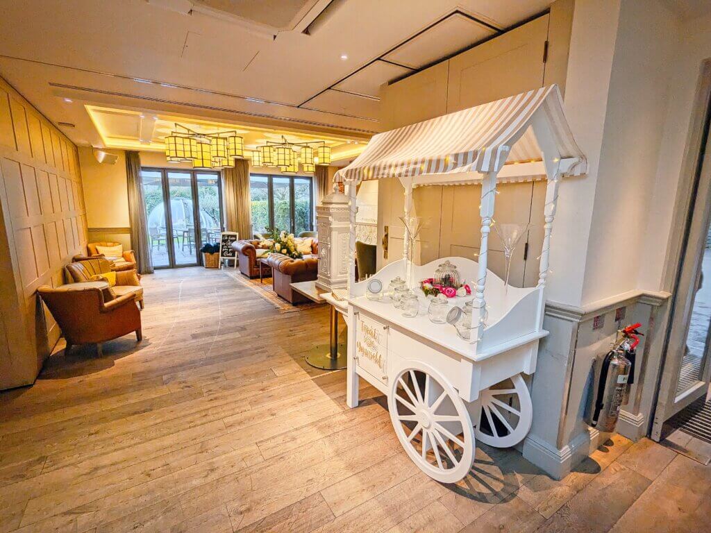 Sweet cart hire with gold and white colour scheme for top canvas, front "Treat Yourself" sign and sweet bags. Lockable wedding post box seen to the left of the sweet cart. Photographed at the Great House in Sonning, Berkshire