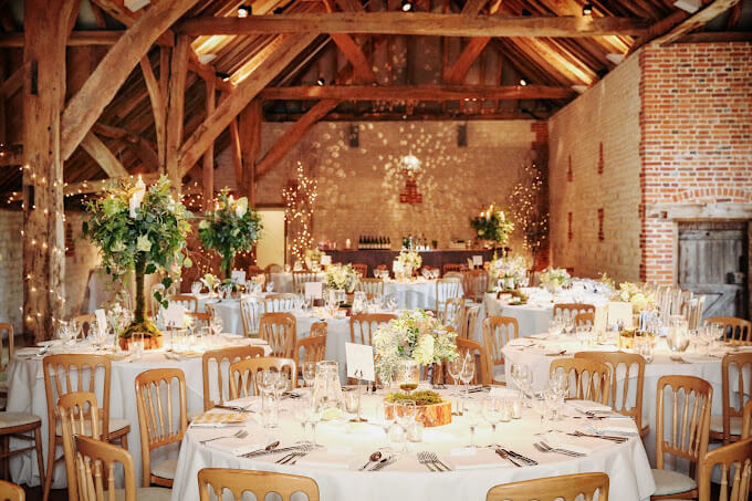 The barn at bury court in Bentley, Surrey. Many round tables are set and decorated inside the main barn with the bar visible in the background