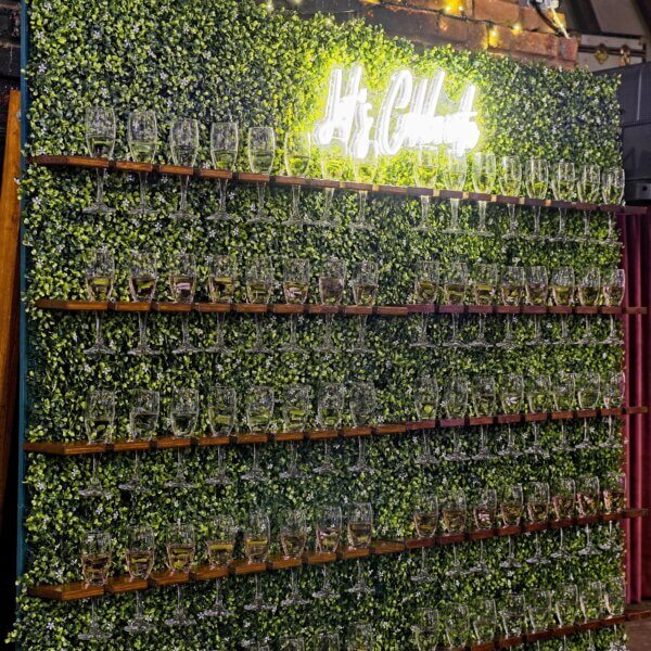 Large double prosecco wall with green boxwood backing, filled with 96 glasses.