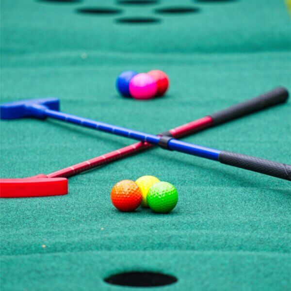 Closeup of a red and a blue adjustable putters and 6 coloured golf balls sitting on a putting mat