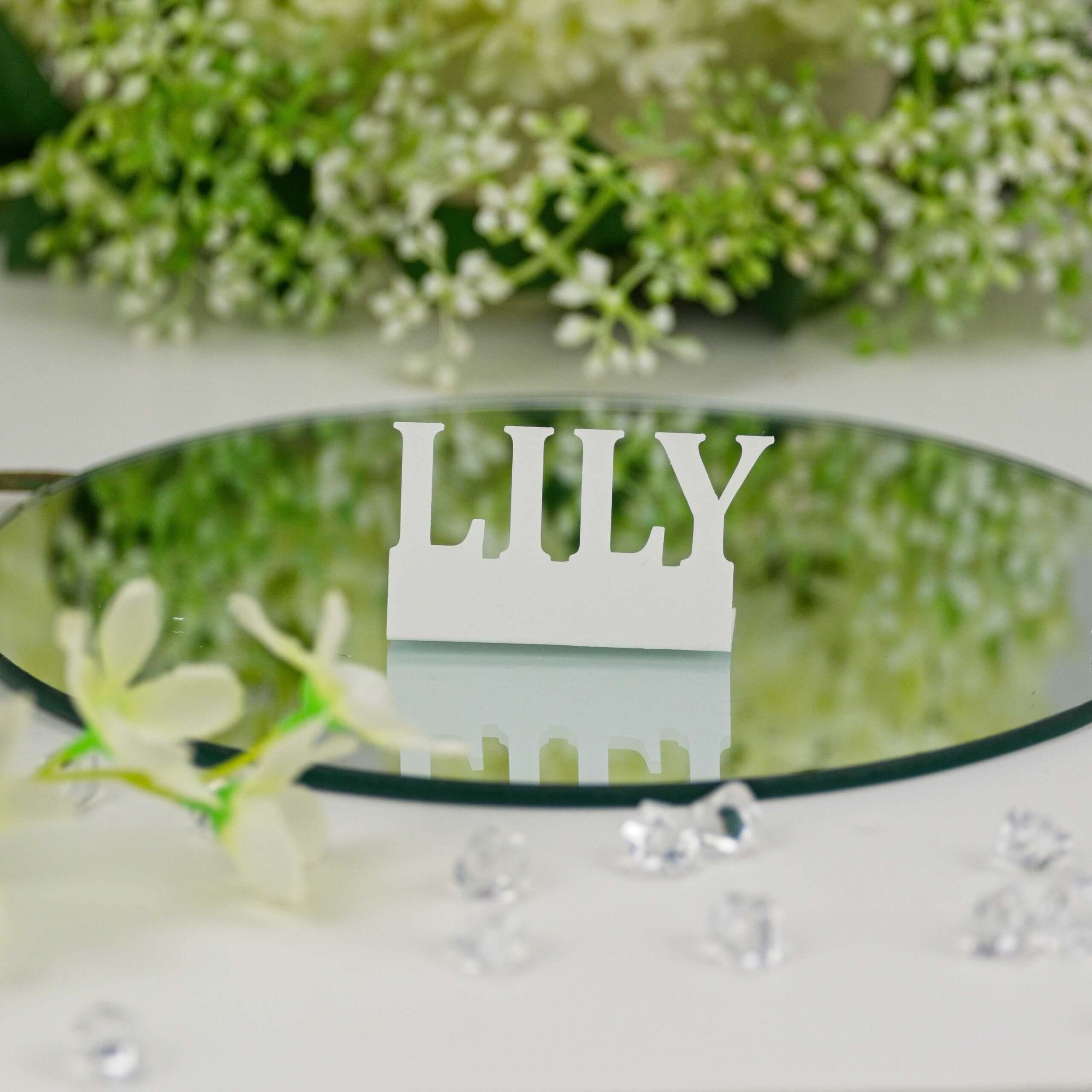 White "LILY" standing name cut-out on round mirror with white flowers and crystal accents, front view.
