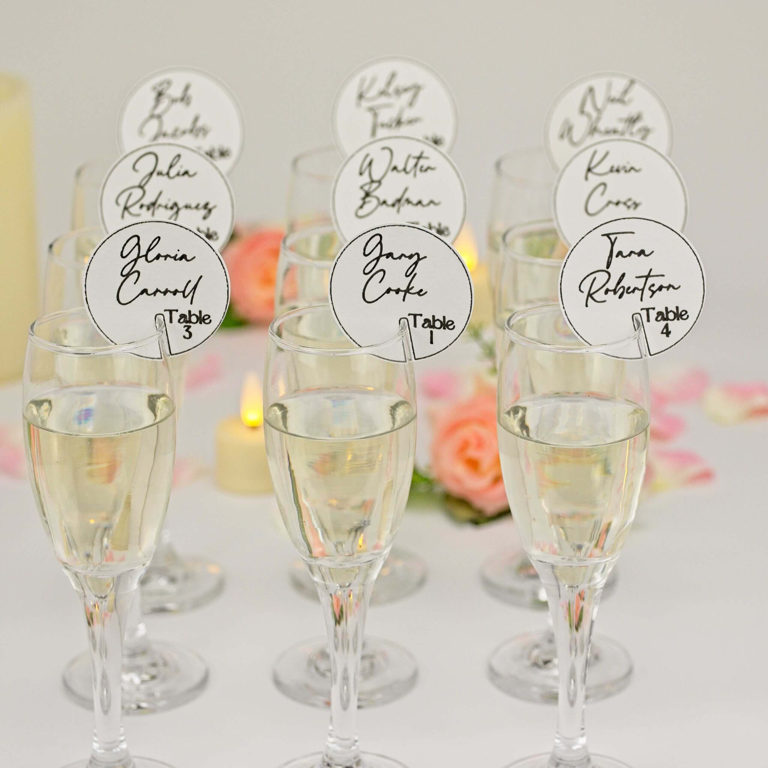 Cluster of champagne flutes with round white seating tags; floral bokeh