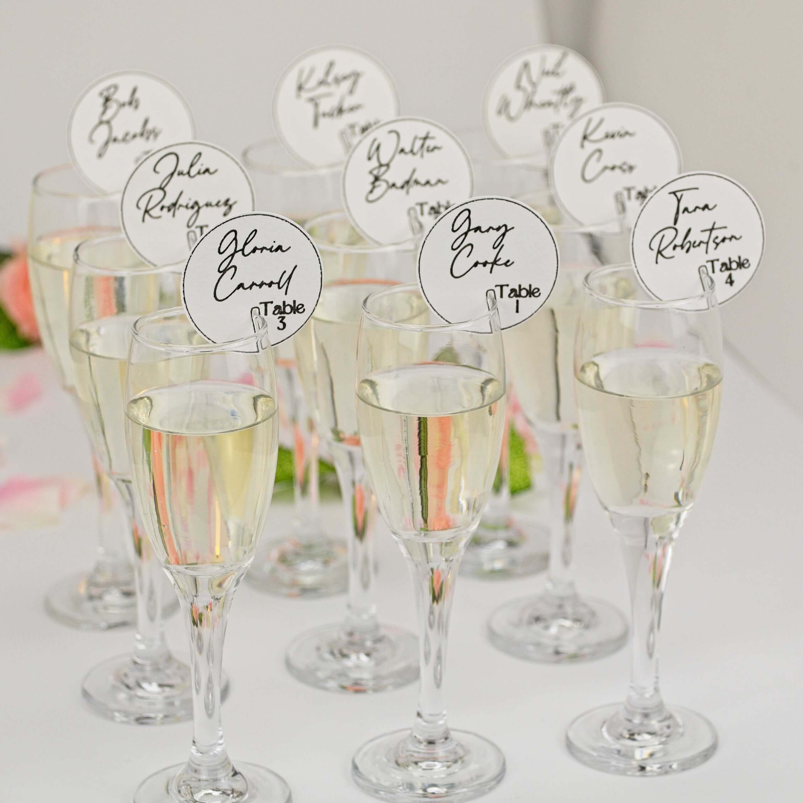 Cluster of champagne flutes with round white seating tags; floral bokeh