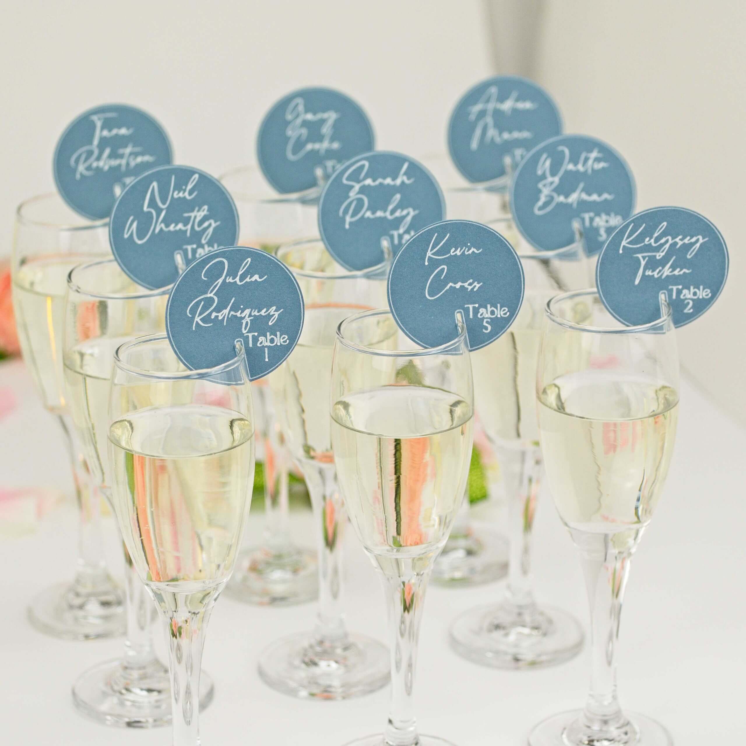 Cluster of flutes each with blue round seating tags; soft floral bokeh
