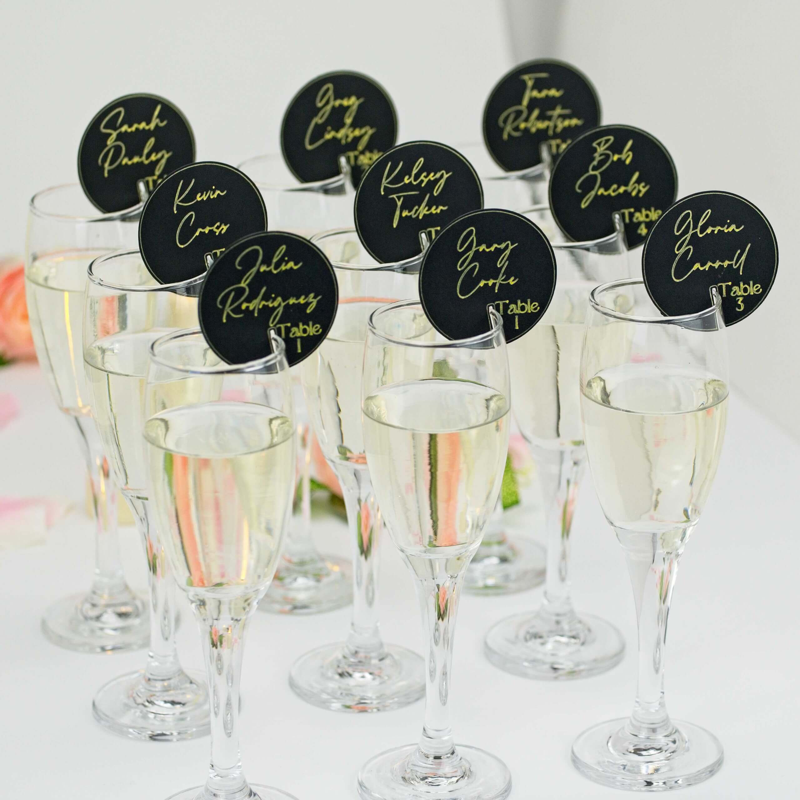 Cluster of champagne flutes with black round seating tags; rose bokeh