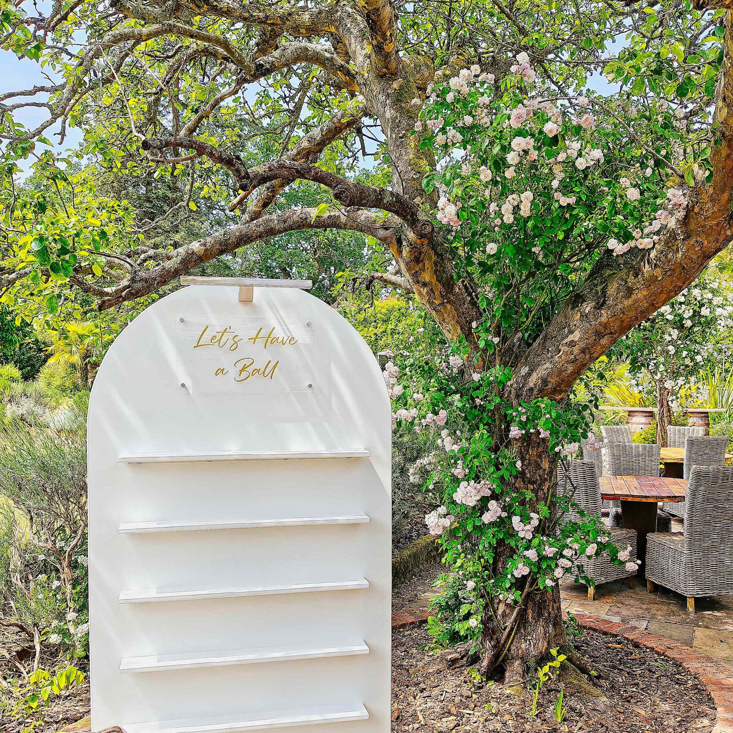 White Shot wall with custom "Let's Have a Ball" sign at the top. The wall is sitting next to a blossom tree.